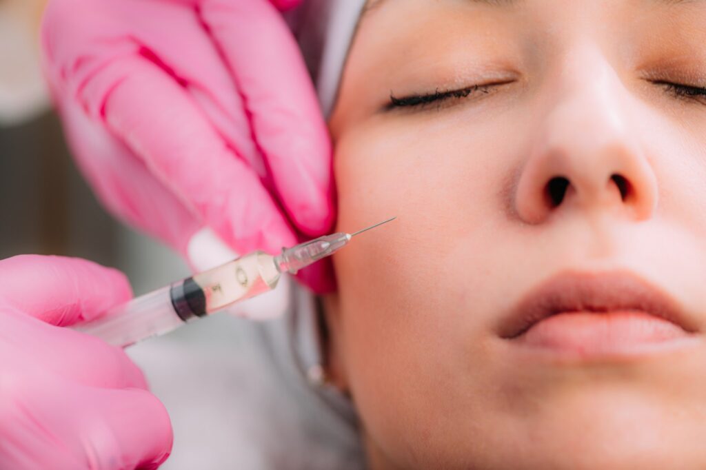 Close-up of a patient's cheek receiving a dermal filler injection, with the medical professional wearing pink gloves, emphasizing precision and care in cosmetic treatment.